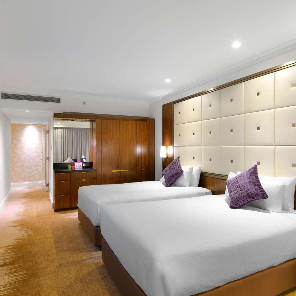 Amora Hotel Jamison Sydney Cameră foto The photo shows a modern hotel room featuring two twin beds with white bedding and purple decorative pillows. The walls are designed with soft beige panels, creating a luxurious ambiance. There’s wooden furniture, including a cabinet against one wall